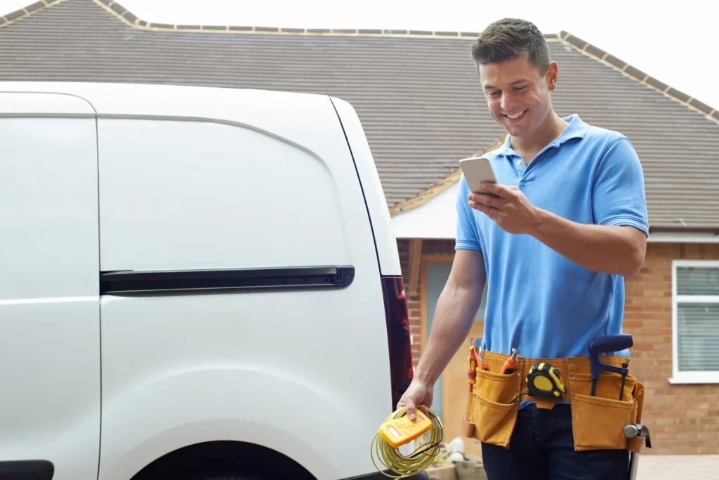 Smiling builder looking at phone and smiling while standing outside next to white van