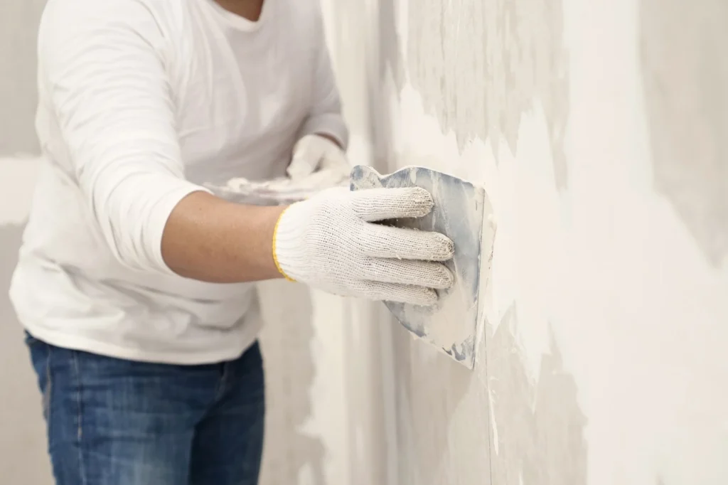 Close up of persons hand patching up white wall with putty